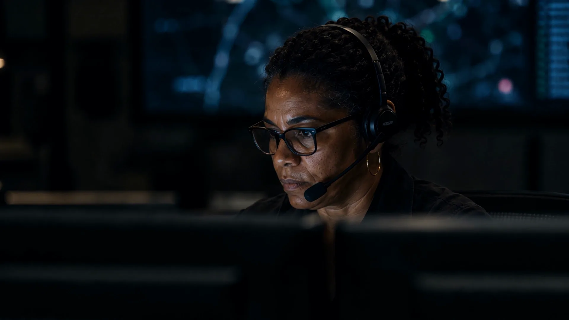 The coordination center in the film: a small dark room, one operator leaning toward her monitor.