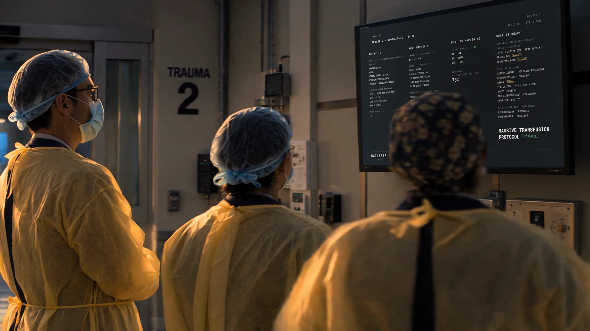 The trauma team in yellow gowns and masks, backs to camera, reading the wall display together.