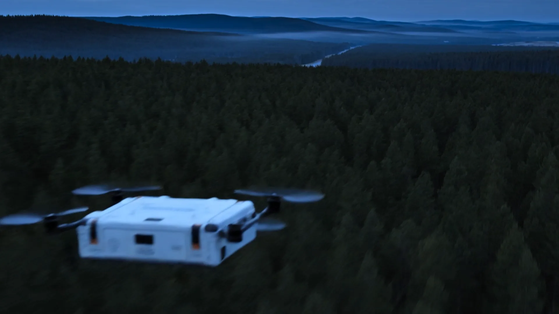 An early test frame: a white box-shaped drone with rotors flying over a forest.