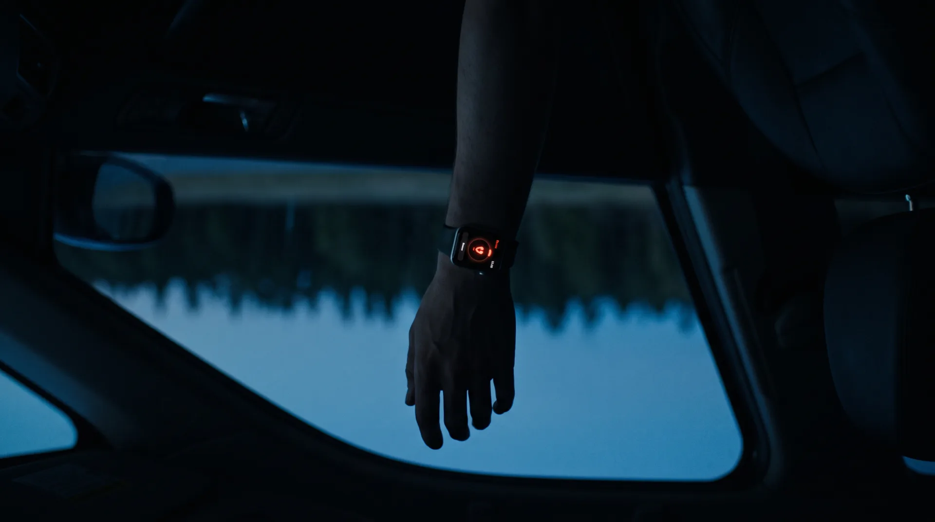 The watch in the film: a hand hangs limp beside the door in blue pre-dawn light, the watch face a small red mark.